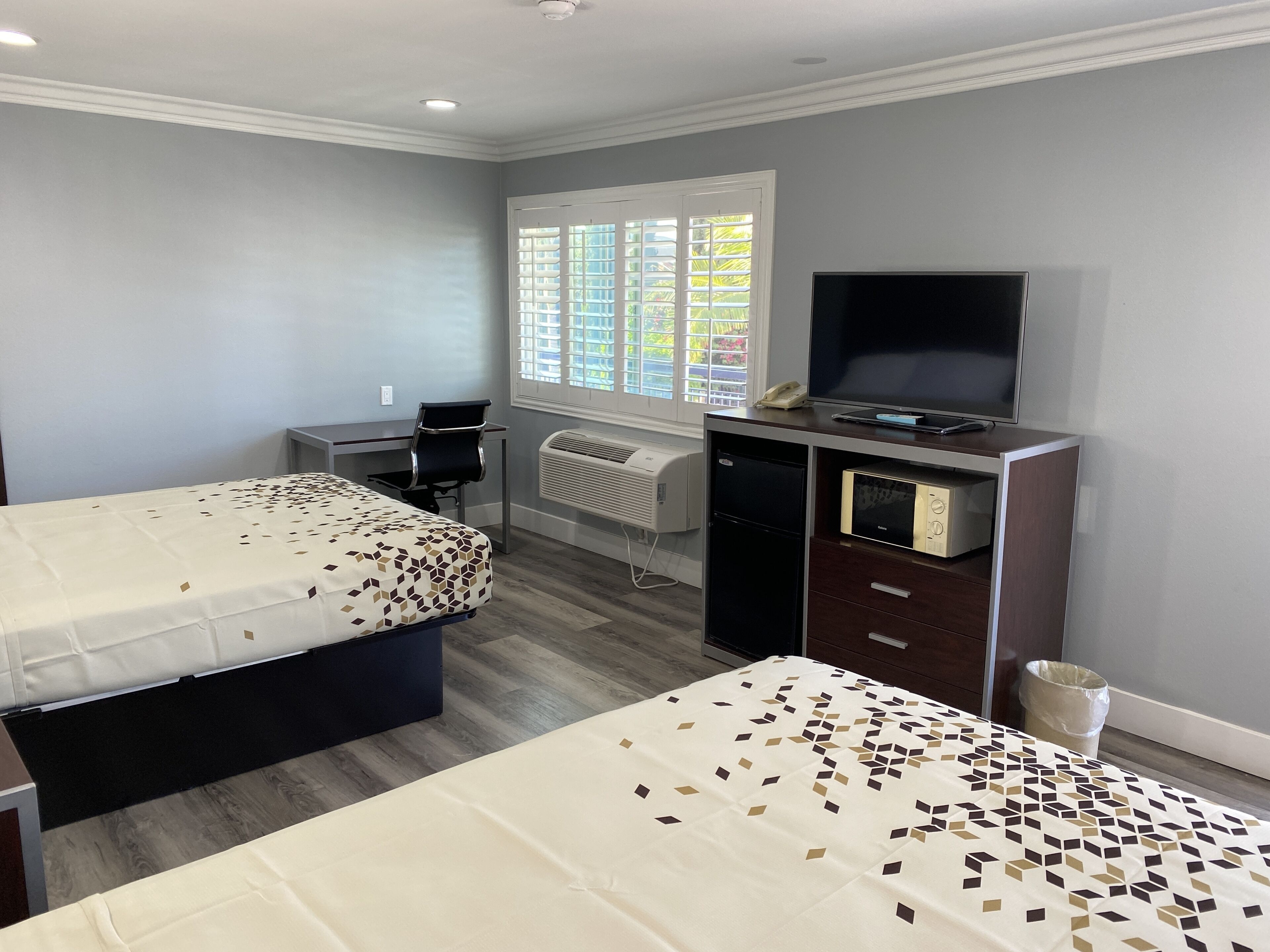 A hotel room with two beds, a desk with a computer, a TV, and a window with blinds.