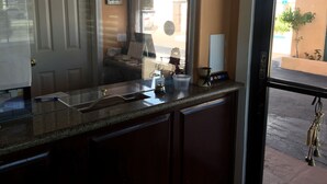 A kitchen counter with a coffee machine, a small plant, and a window with a view of the street. - Regency Motel of Brea (Brea)