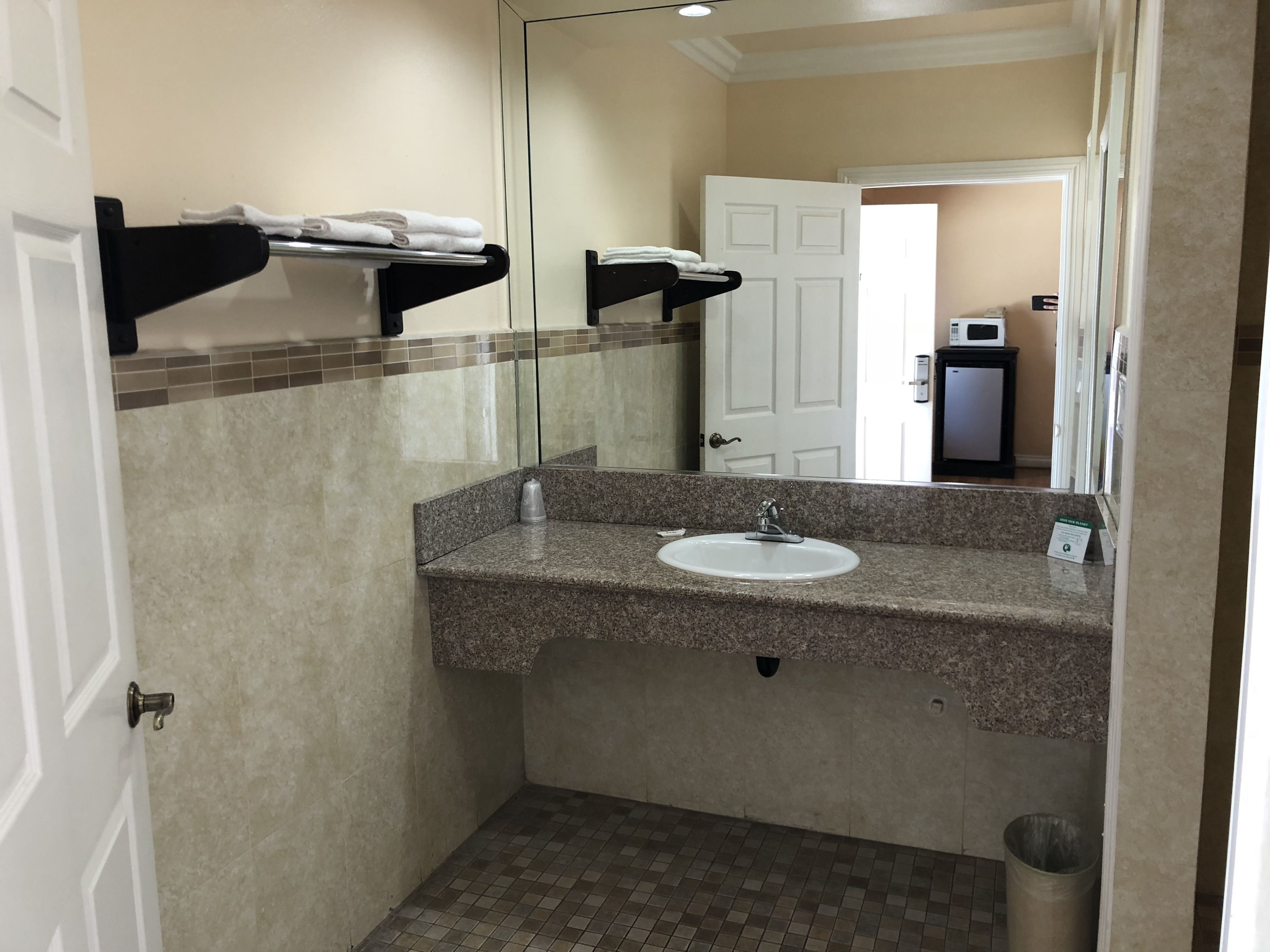 A bathroom with a granite countertop sink, a mirror, a towel rack, and a trash can.