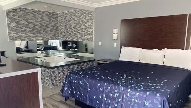 A modern hotel room with a large bed, a built-in desk, and a bathroom with a mirror and sink. - Regency Motel of Brea (Brea)