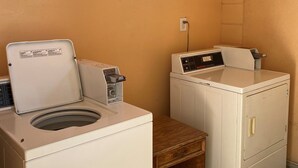 A laundry room with two washing machines, a small wooden table, and a notice board with laundry instructions. - Regency Motel of Brea (Brea)