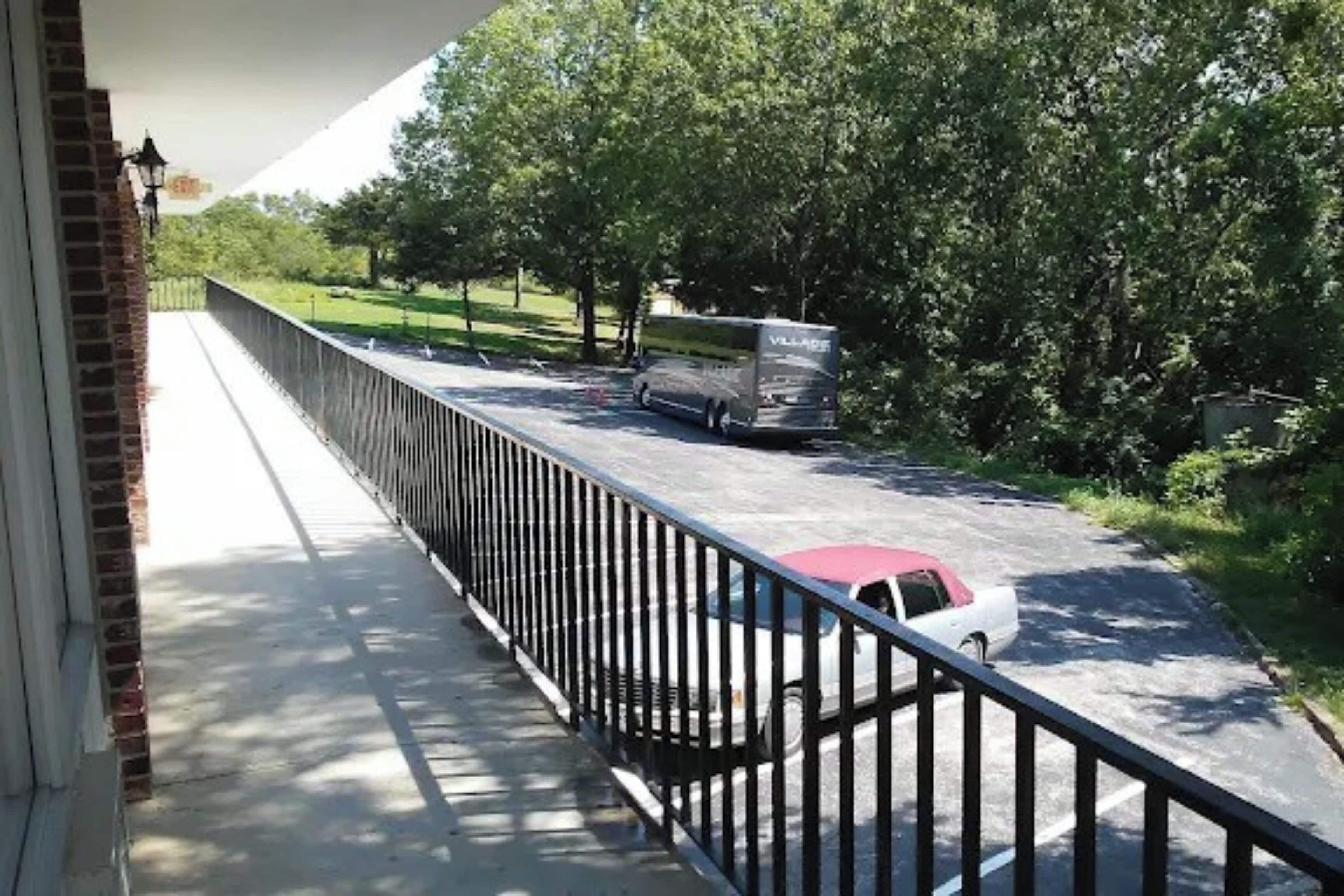 Un balcón con vistas a una calle, un coche estacionado y un autobús.