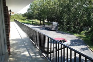 A balcony with a view of a road, a parked car, and a bus.