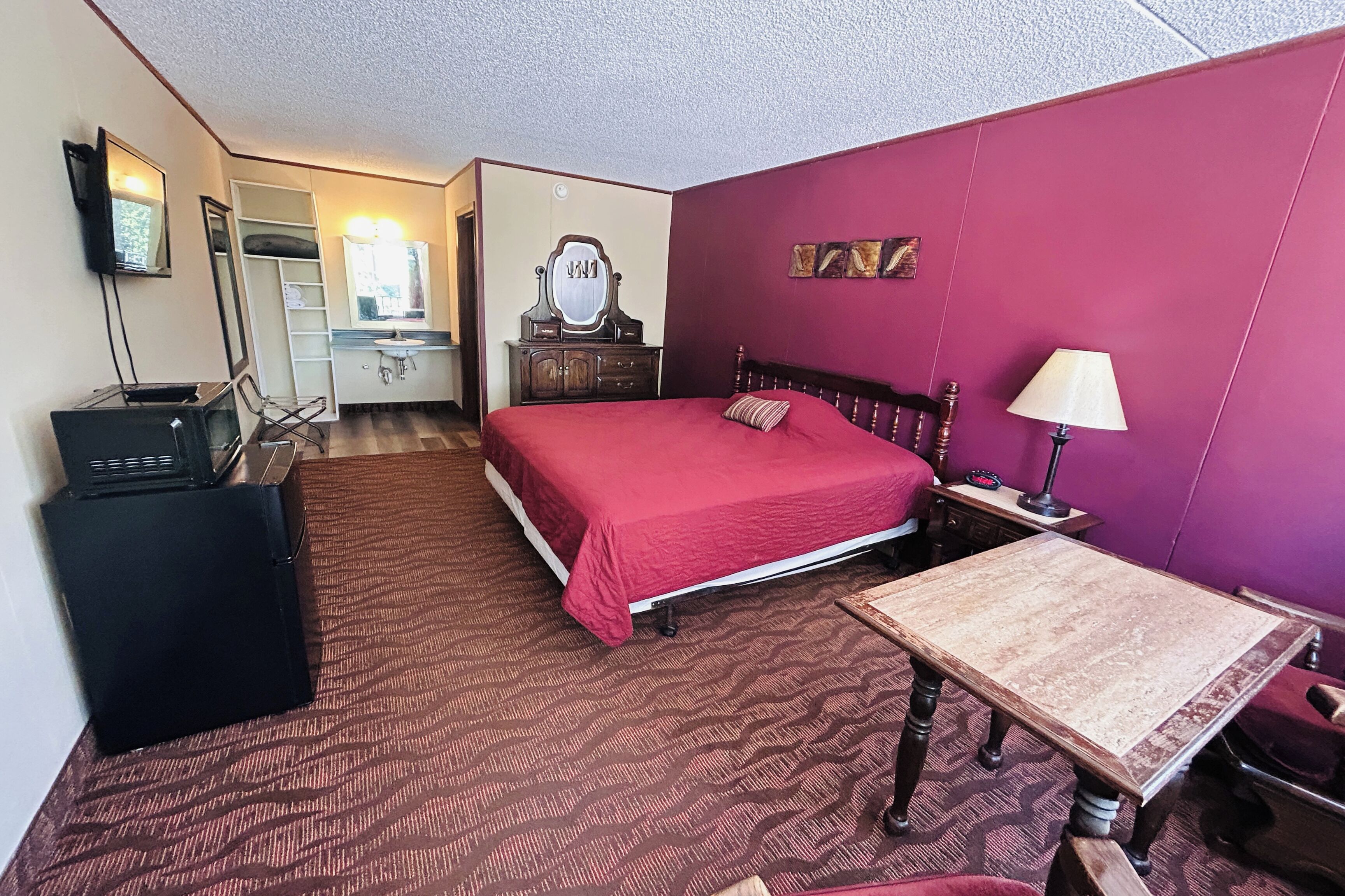 Habitación de hotel con cama, escritorio, cómoda, espejo y televisor.