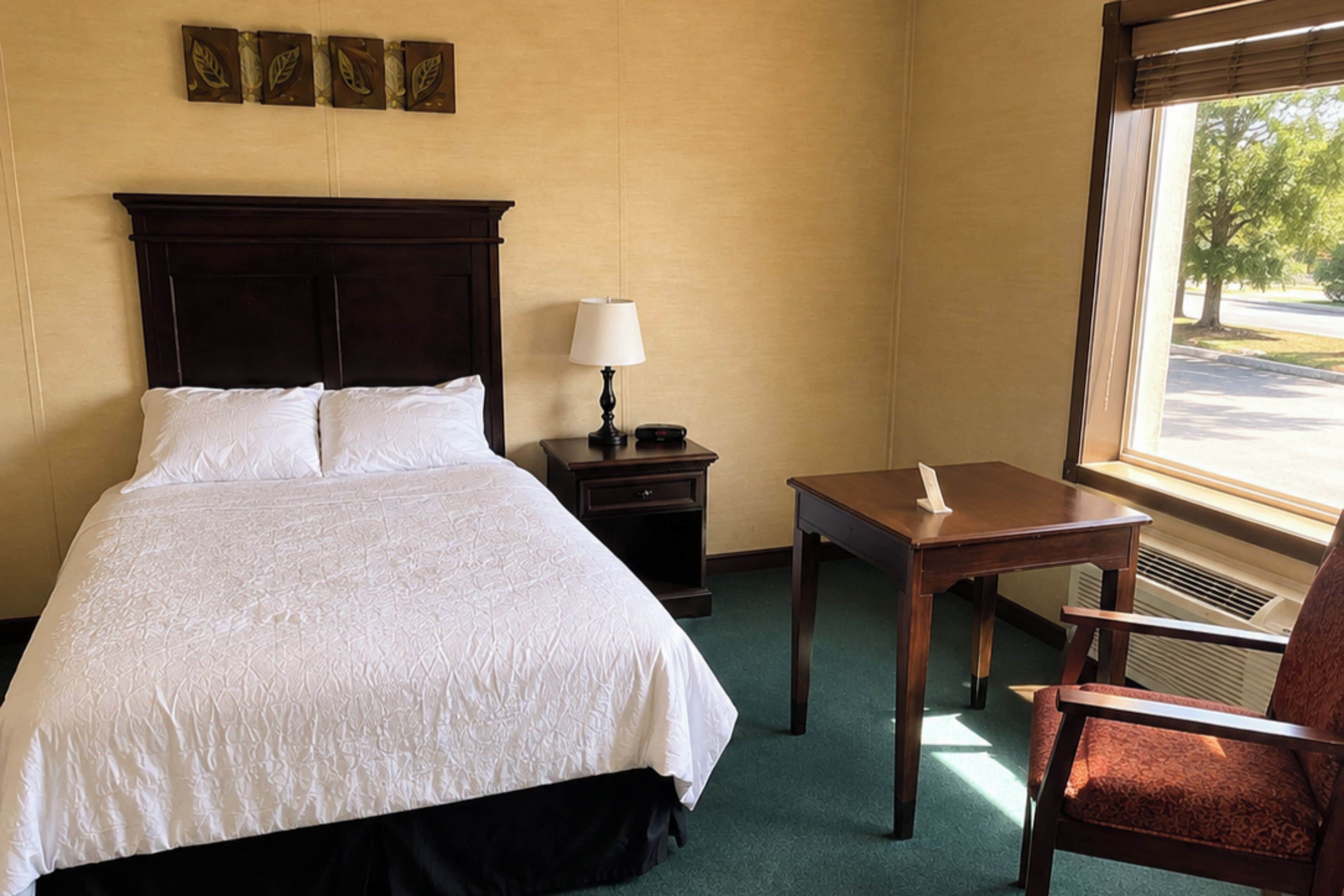Une chambre d’hôtel avec un grand lit, une table de chevet avec une lampe, une petite table et une chaise.