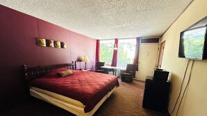 Una camera d'albergo con un letto grande, una scrivania con una sedia, una televisione e una finestra con tende.