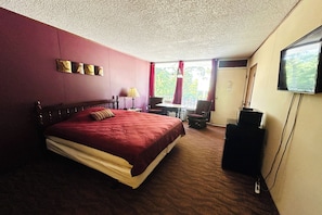 A hotel room with a large bed, a desk with a chair, a television, and a window with curtains. - Colonial Mountain Inn Branson MO (Branson West)