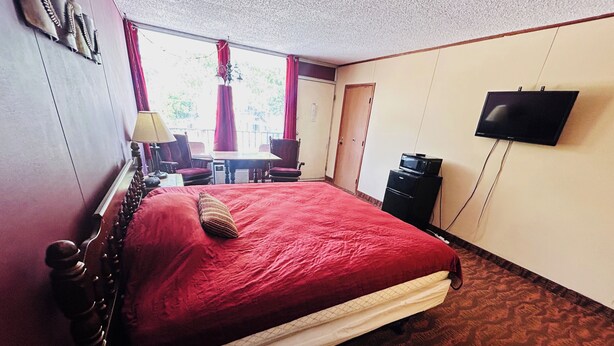 Una camera d'albergo con un letto grande, televisione, una scrivania con sedia e finestra con tende.