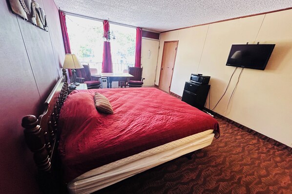 A hotel room with a large bed, a television, a desk with a chair, and a window with curtains. - Colonial Mountain Inn Branson MO (Branson West)