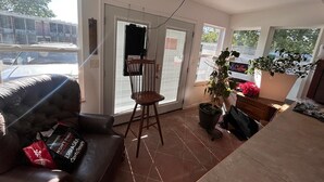 A living room with a sofa, a wooden chair, a ceiling fan, a potted plant, and a view of the outside.