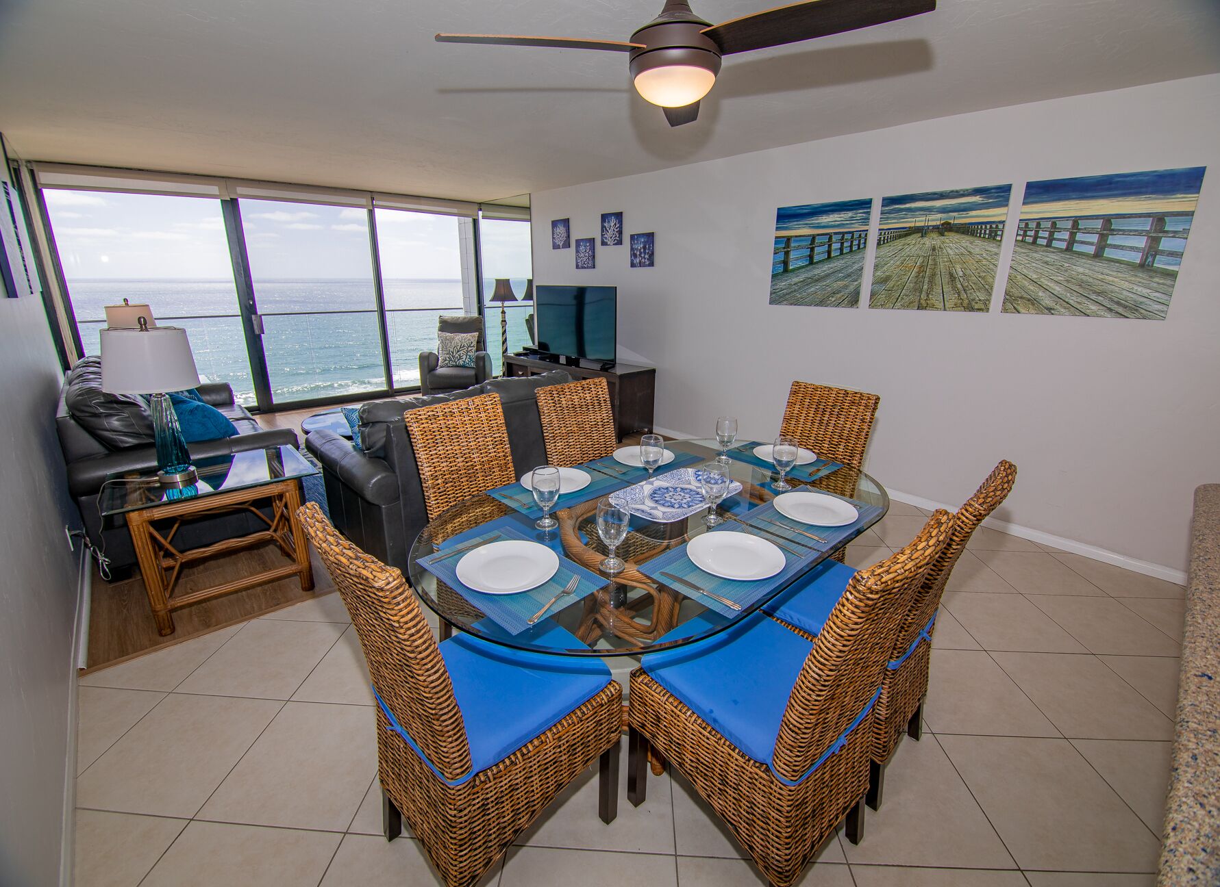 A dining area with a view of the ocean, a ceiling fan, and artwork on the walls.