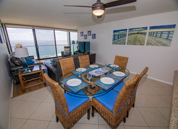 A dining area with a view of the ocean, a ceiling fan, and artwork on the walls. - Capri Beach Accommodations (San Diego)