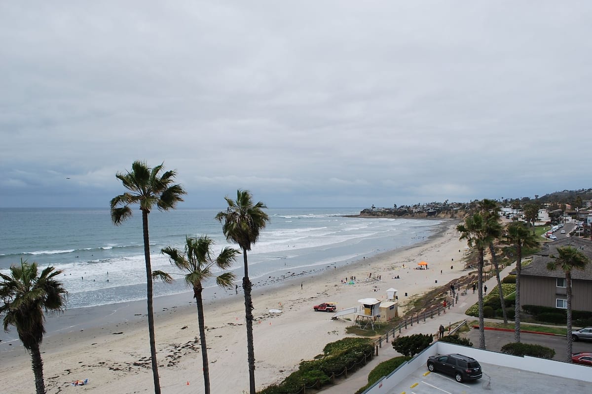A beach with palm trees, a lifeguard tower, and a parking area.