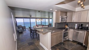 A modern kitchen with granite countertops, stainless steel appliances, and a view of the ocean. - Capri Beach Accommodations (San Diego)
