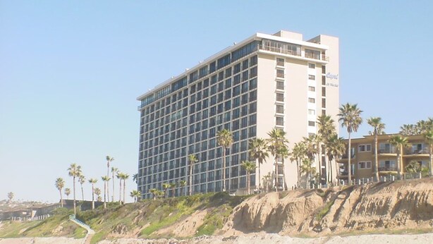 A multi-story hotel with a modern design, located near a beach with palm trees. - Capri Beach Accommodations (San Diego)