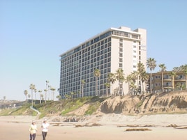 A multi-story hotel with a modern design, located near a beach with palm trees.