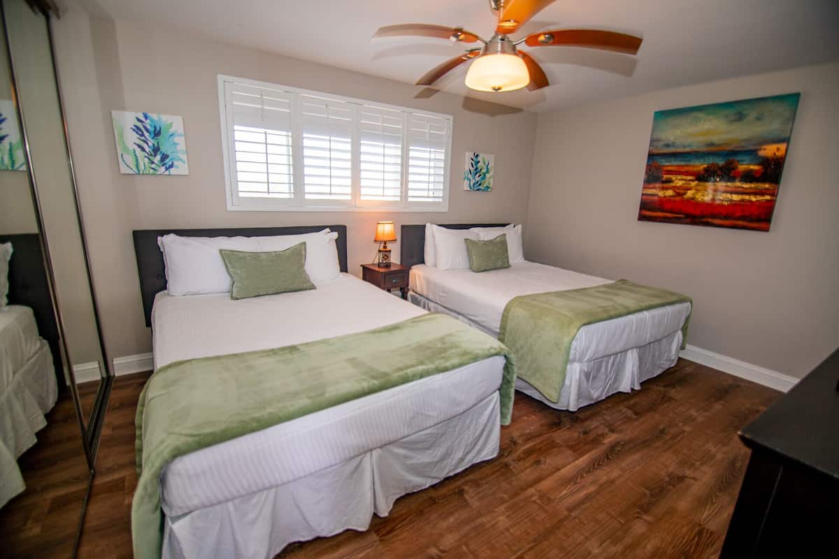 A bedroom with two beds, a ceiling fan, a window with blinds, and a painting on the wall.