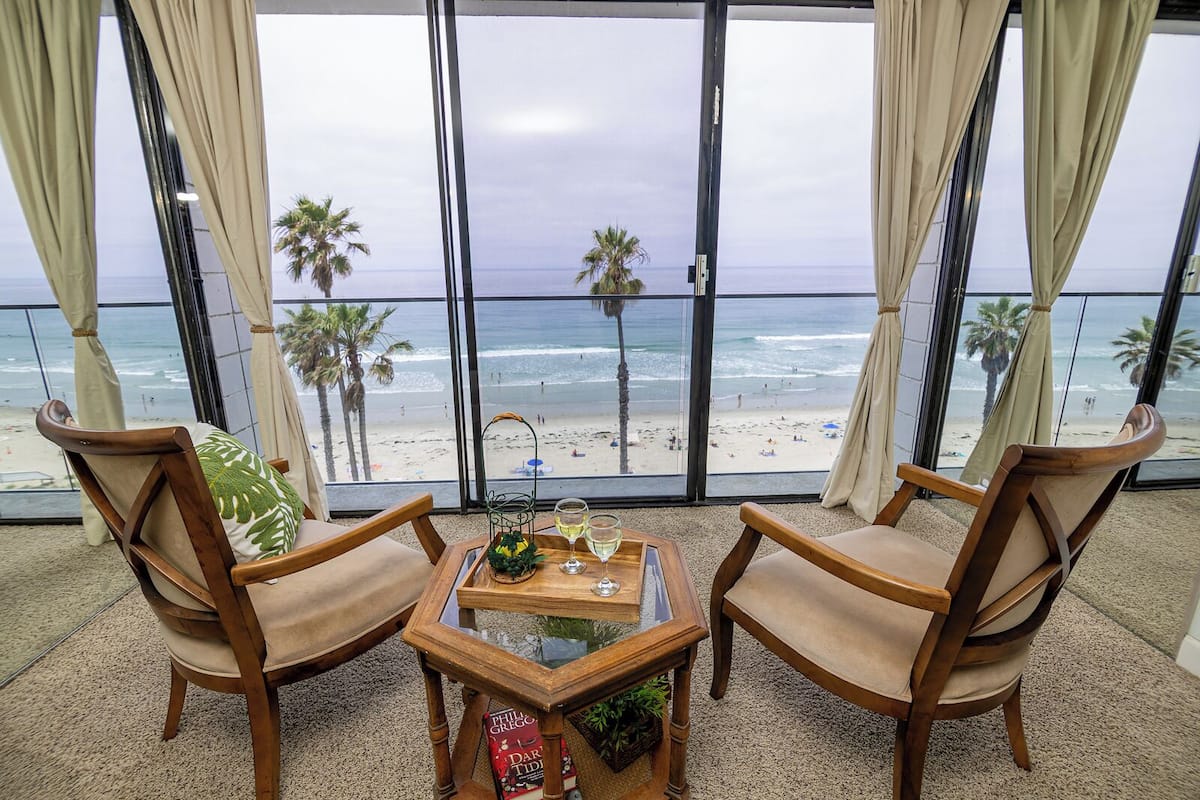 A balcony with two wooden chairs, a small table with a tray, and a view of the beach and ocean.