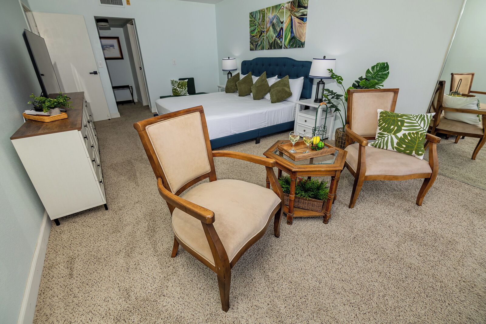 A bedroom with a bed, two chairs, a small table, and a dresser.