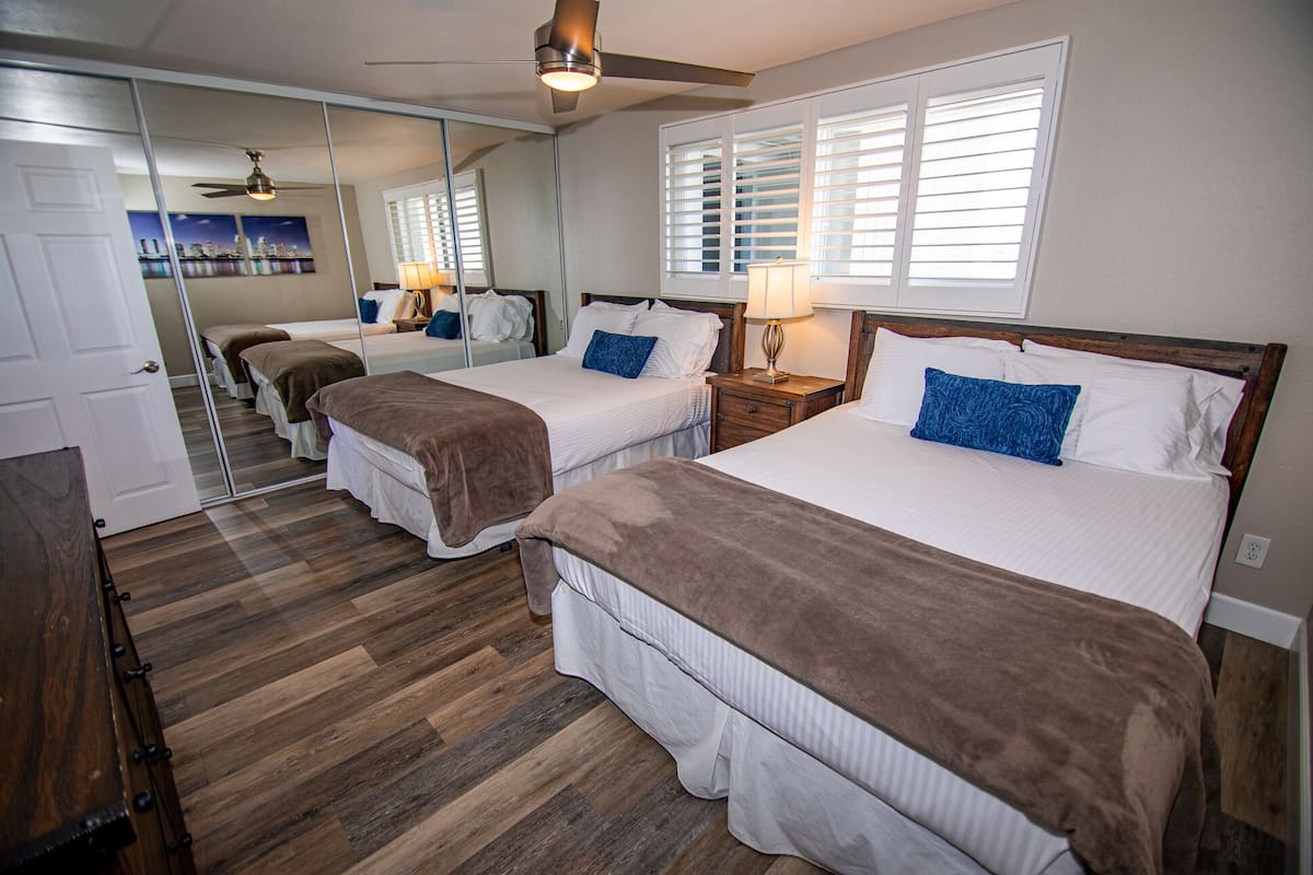 A hotel room with two beds, wooden flooring, a ceiling fan, and a large mirror reflecting the room.