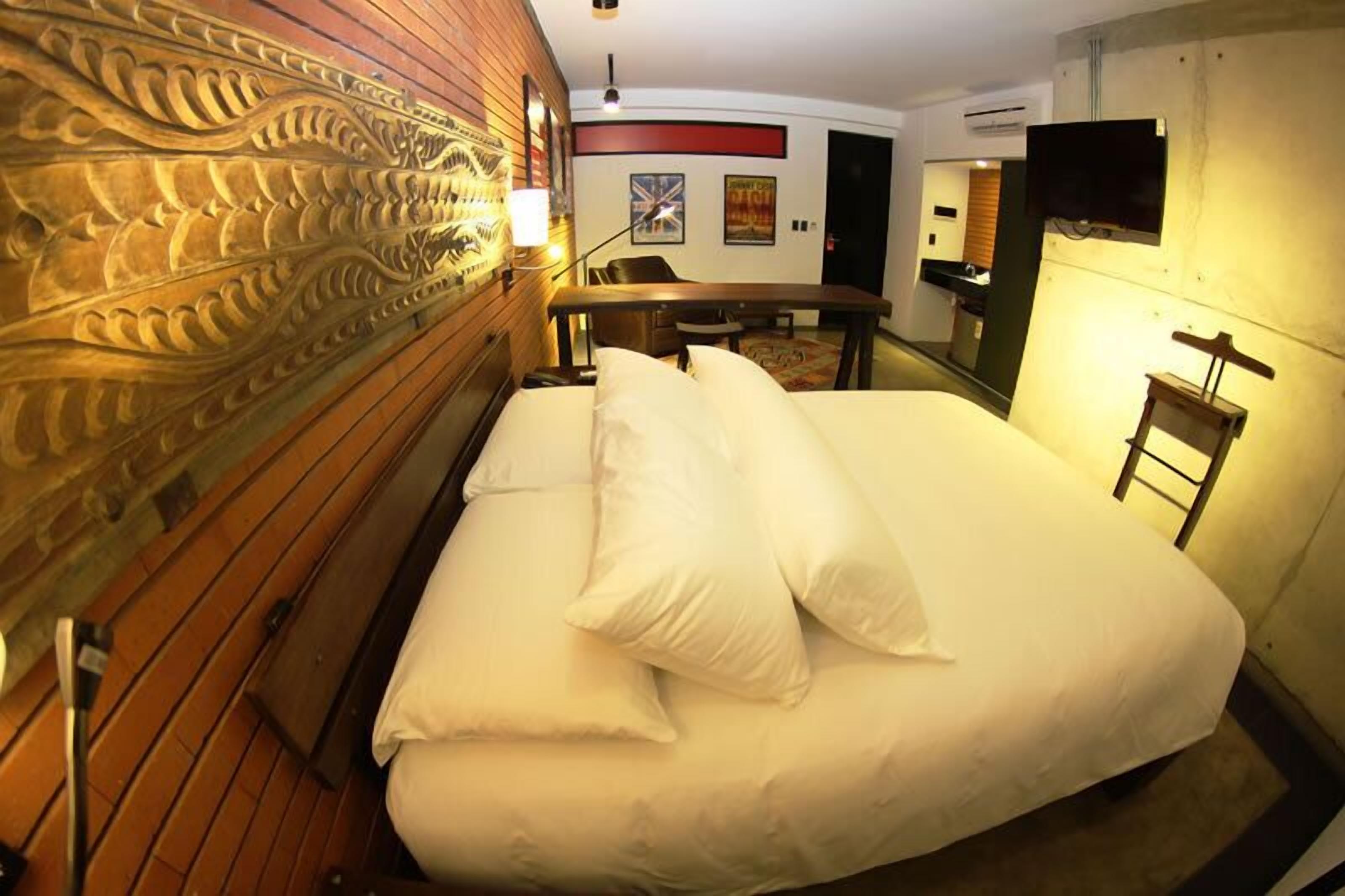 A hotel room with a large bed, a wooden headboard, a desk, and a television mounted on the wall.