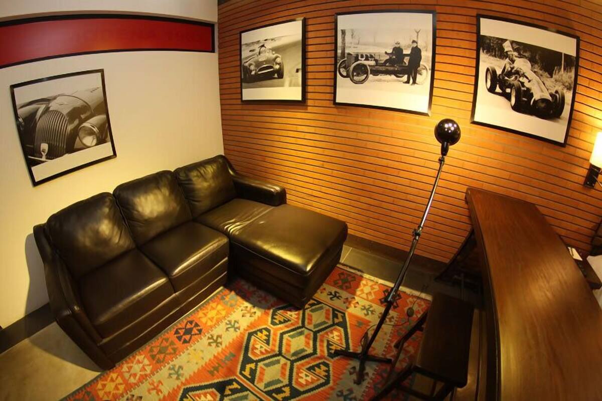 A room with a leather sofa, a patterned rug, and wall-mounted pictures of vintage cars.