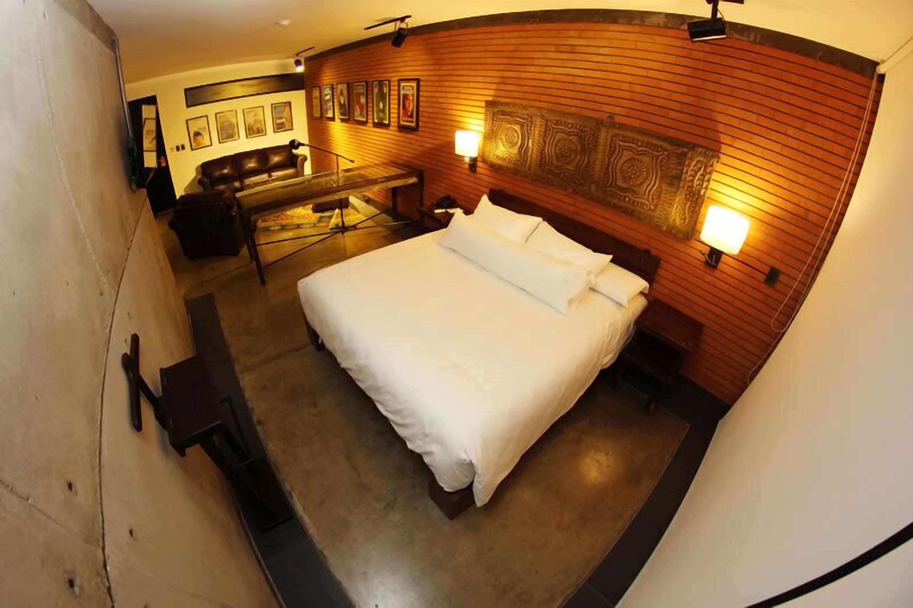 Habitación de hotel con una cama grande, cabecera de madera, zona de estar con sofá y sillones, y televisor de pantalla plana montado en la pared.