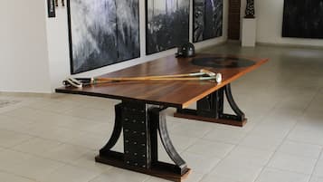 Una mesa de comedor con tapa de madera larga y base de metal negro, ubicada en una habitación con suelo de baldosas y cuadros abstractos en las paredes.