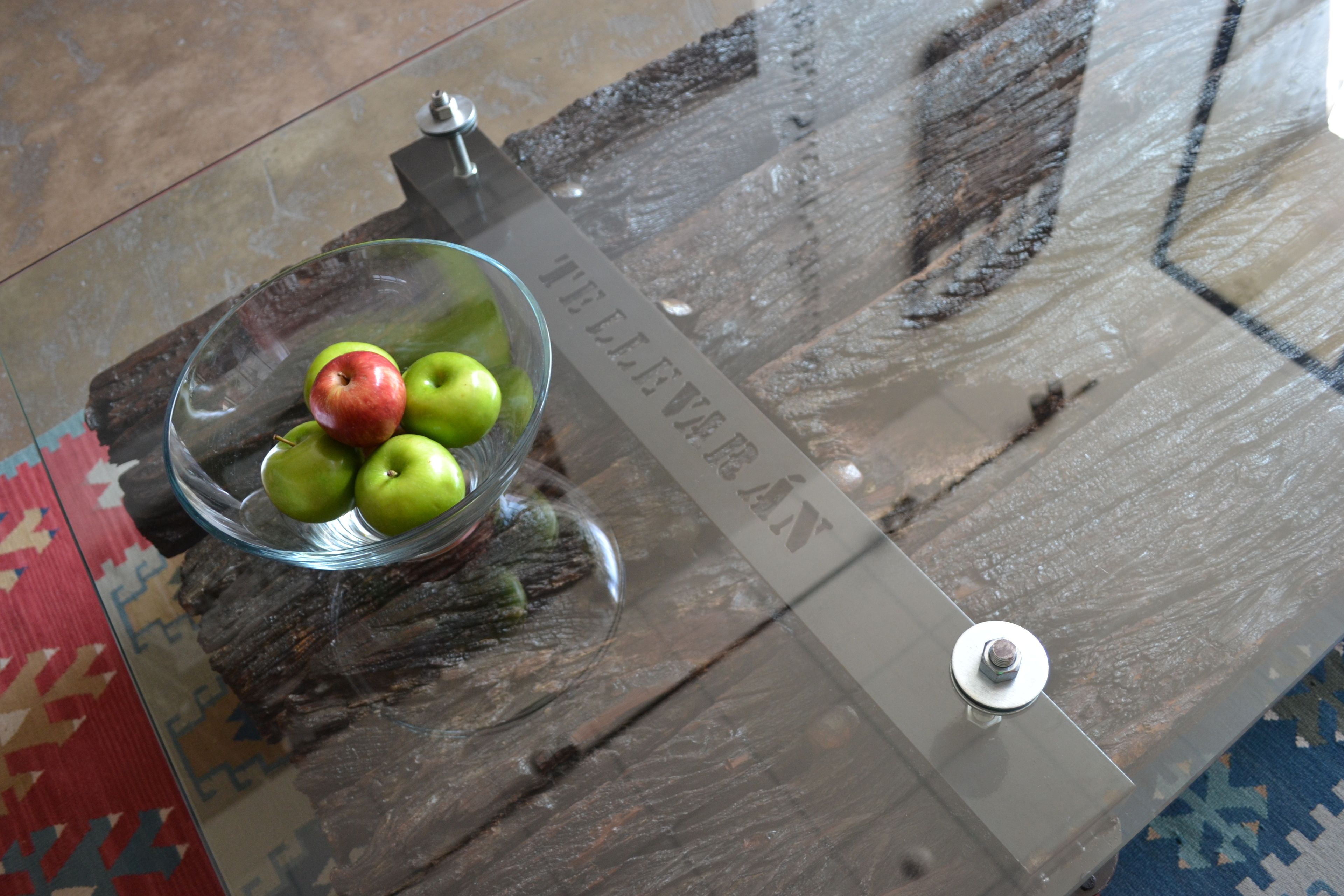 A glass table with a bowl of green apples and a red apple.