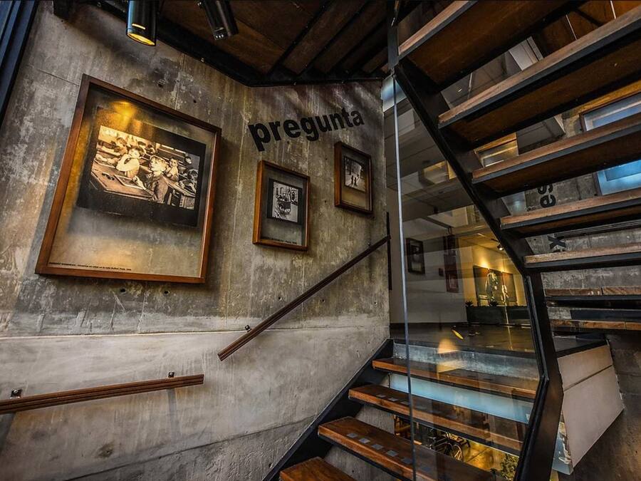 A staircase with a metal railing, wooden steps, and a concrete wall with framed pictures.