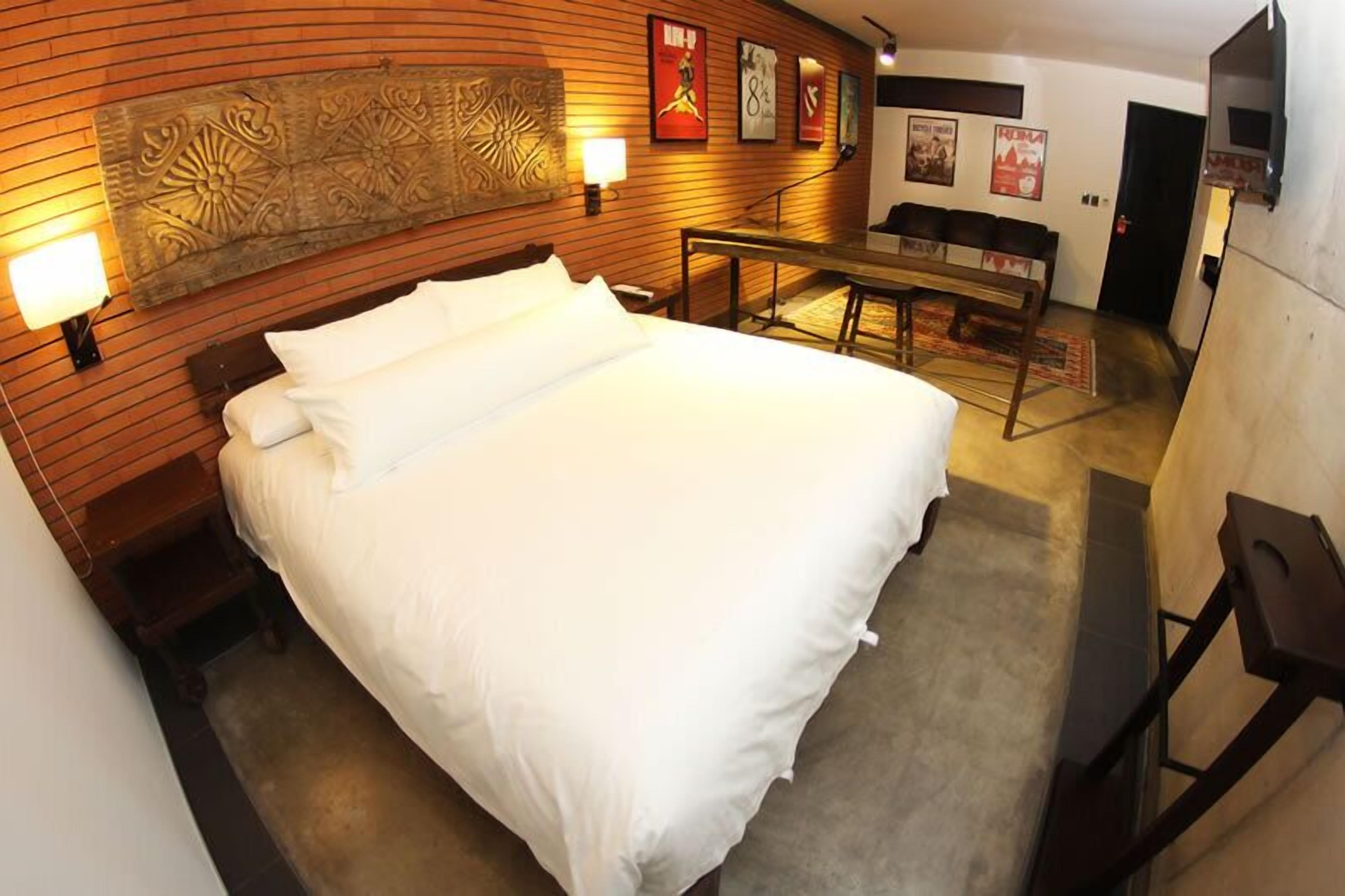Een hotelkamer met een groot bed, een houten hoofdbord, een bankje en een aan de muur bevestigde televisie.