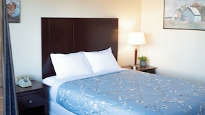 A hotel room with a bed, a nightstand, a lamp, and a painting on the wall. - Stagecoach Inn (Molalla)