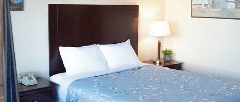 A hotel room with a bed, a nightstand, a lamp, and a painting on the wall.