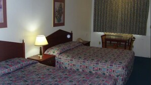 A hotel room with two beds, a nightstand with a lamp, a chair, and a window with curtains. - Stagecoach Inn (Molalla)