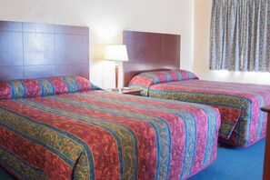 Habitación de hotel con dos camas, una mesita de noche, una lámpara y una ventana con cortinas.
