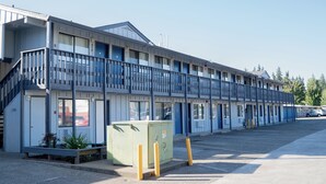 A motel with a two-story structure, a covered parking area, and a small green utility box. - Stagecoach Inn (Molalla)