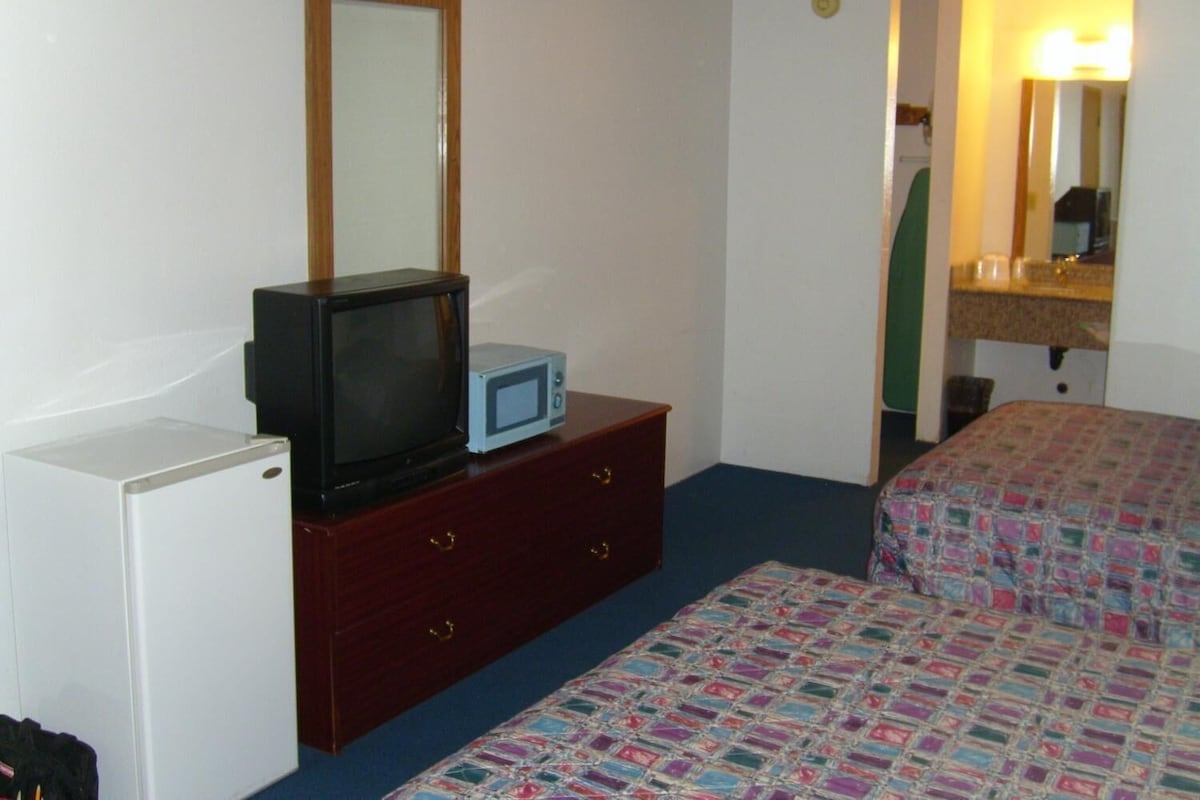 Quarto de hotel com uma cama, penteadeira com televisão e micro-ondas, pequeno frigorífico e espelho.