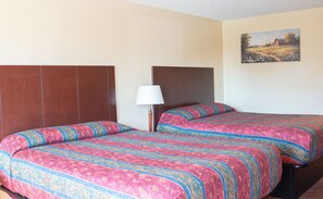 Habitación de hotel con dos camas, una mesita de noche, una lámpara y un cuadro en la pared.