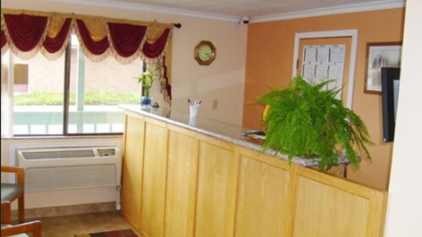 A kitchen with wooden cabinets, a window with red curtains, a clock on the wall, and a potted plant. - Stagecoach Inn (Molalla)