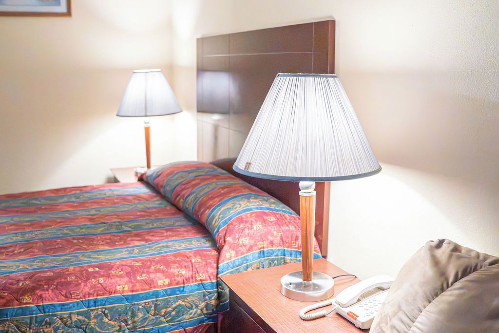A hotel room with a bed, two bedside lamps, a telephone, and a headboard.
