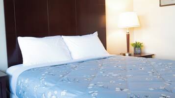 A neatly made bed with a floral-patterned bedspread and two pillows, a bedside lamp, and a small plant on a nightstand.