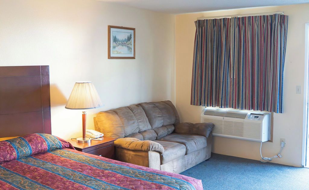 A hotel room with a bed, a sofa, a lamp, a picture on the wall, and a window with curtains.