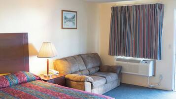 A hotel room with a bed, a sofa, a lamp, a picture on the wall, and a window with curtains.