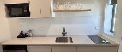 Una cocina moderna con microondas integrado, un lavamanos de acero inoxidable y una estantería para vinos.