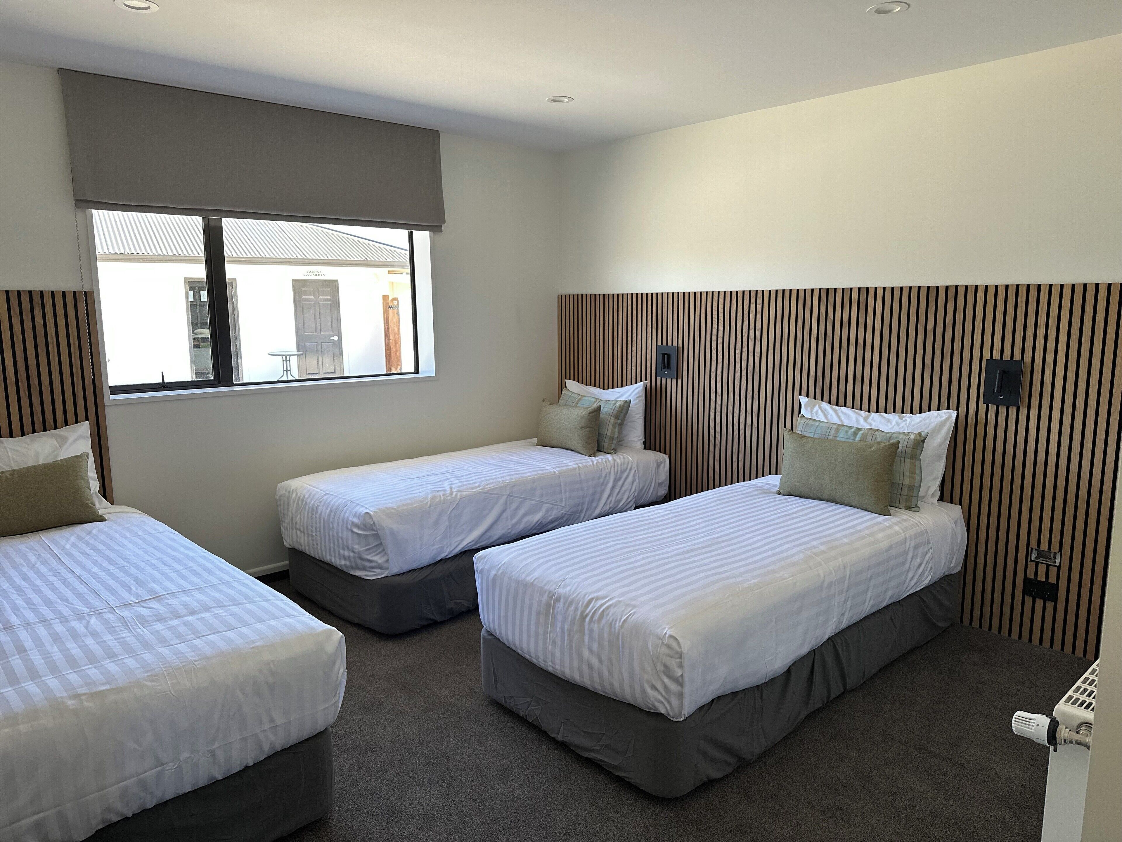 A hotel room with three single beds, a large window with a view, and a wooden headboard.