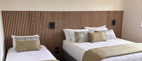 Deux lits simples avec des têtes de lit, un mur recouvert de lambris en bois et un sol recouvert de moquette.