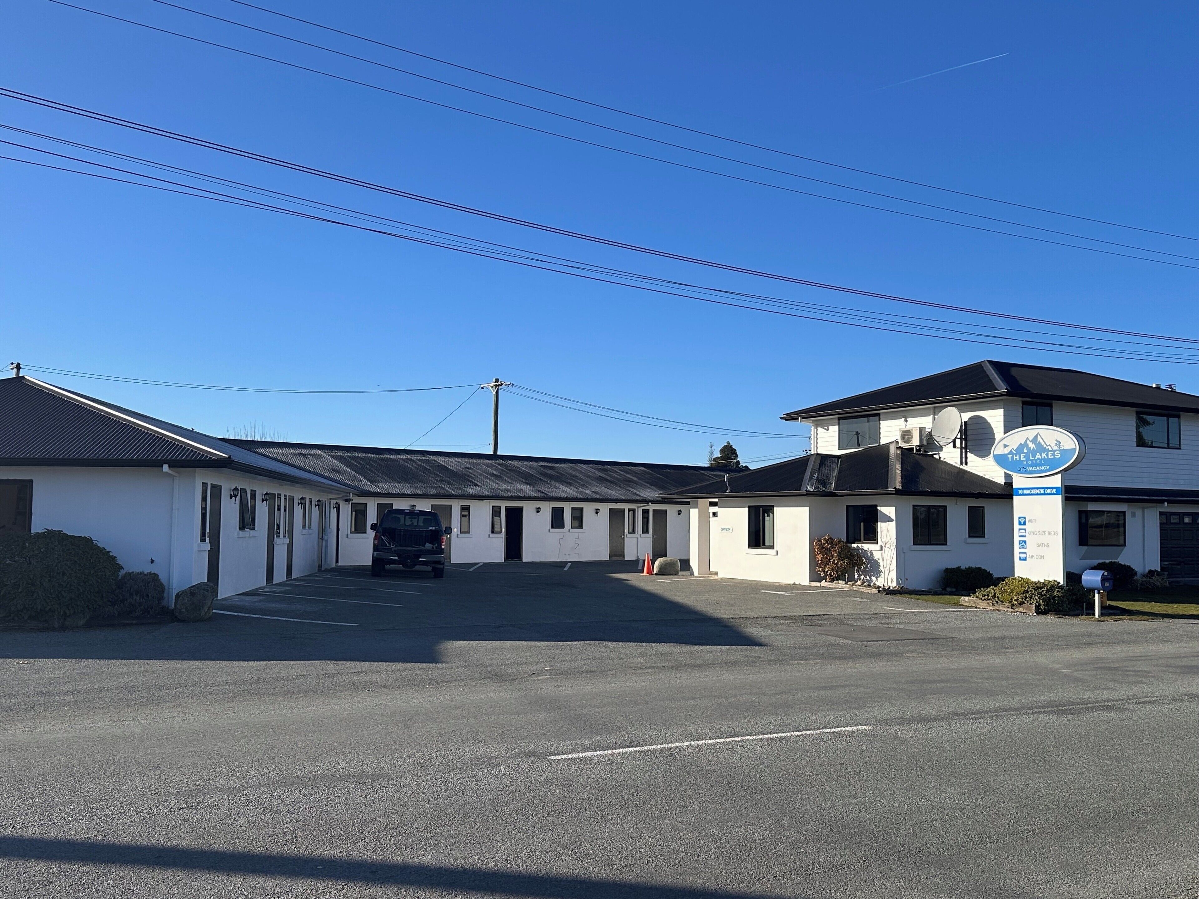 A motel with a parking lot, a sign indicating amenities, and a building with a satellite dish.