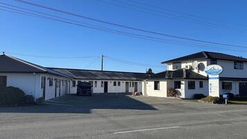 A motel with a parking lot, a sign indicating amenities, and a building with a satellite dish.