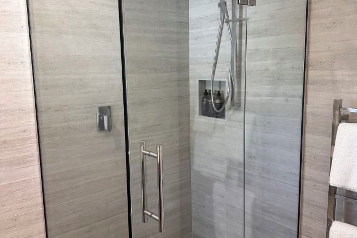 A modern bathroom with a glass shower enclosure, a towel rack, and a built-in soap dispenser.