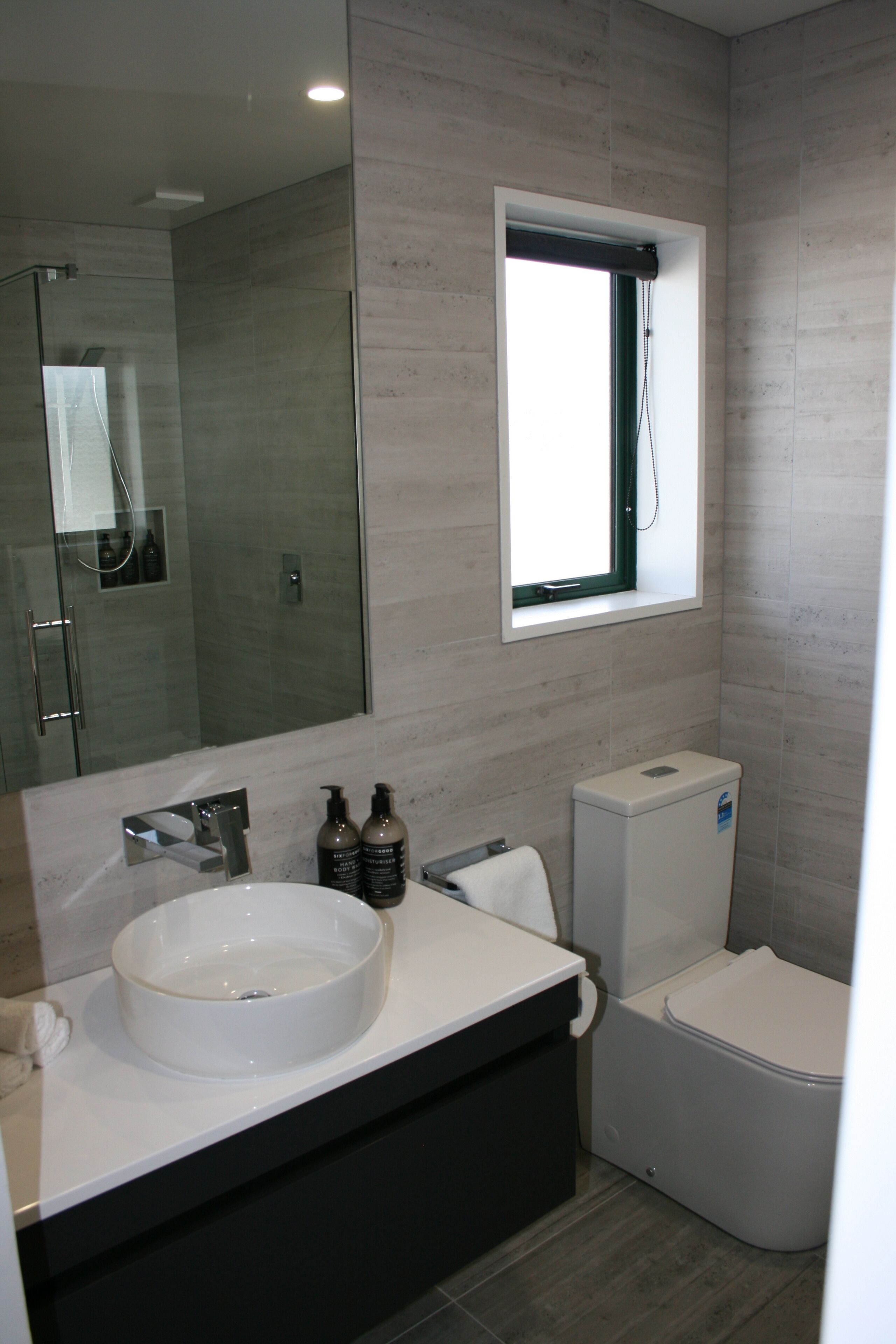 Un baño moderno con un espejo grande, un lavabo, un inodoro y una ducha.